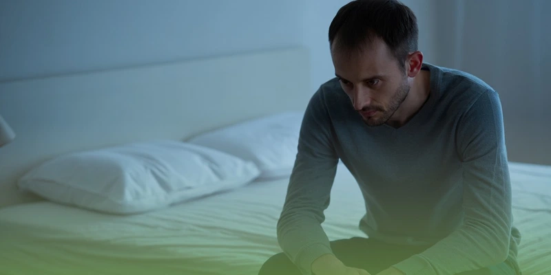 Мужчина с маниакально-депрессивным психозом сидит на кровати 